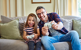 Photo of a father and daughter enjoying playing video games together on a couch.